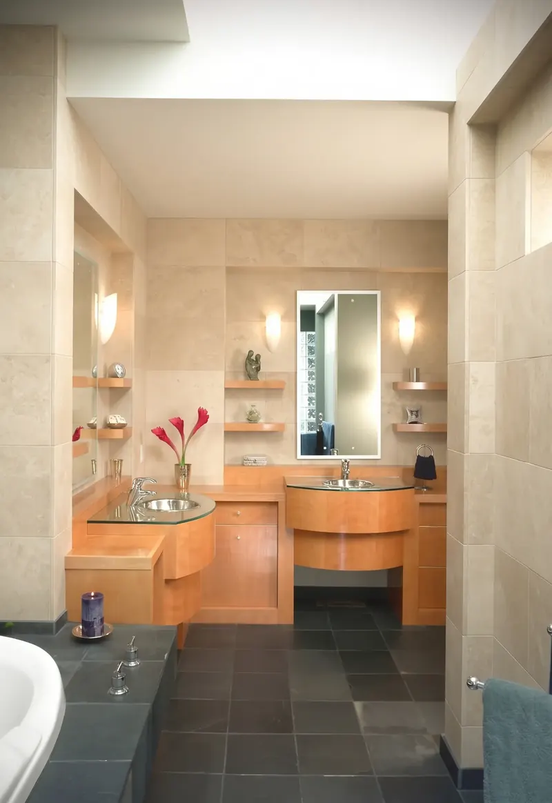 Bathroom with stone-tiled walls, curved wood vanities with glass tops, floating shelves, a dark tile floor and a soaking tub
