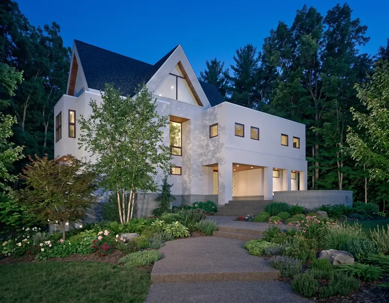White house with steep gables at twilight, a garden path and steps leading up to a lit, columned entry porch