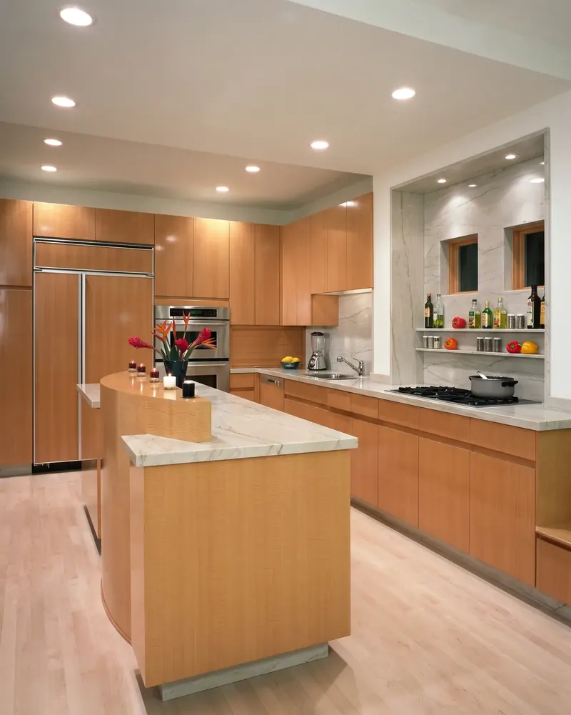 Kitchen with warm wood cabinetry, a curved island with veined stone counters, and a recessed stone-lined cooking alcove
